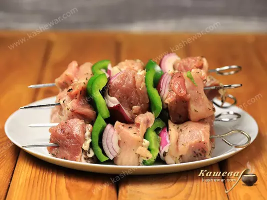 Raw pork kebab on a metal skewer with onions and sweet bell pepper